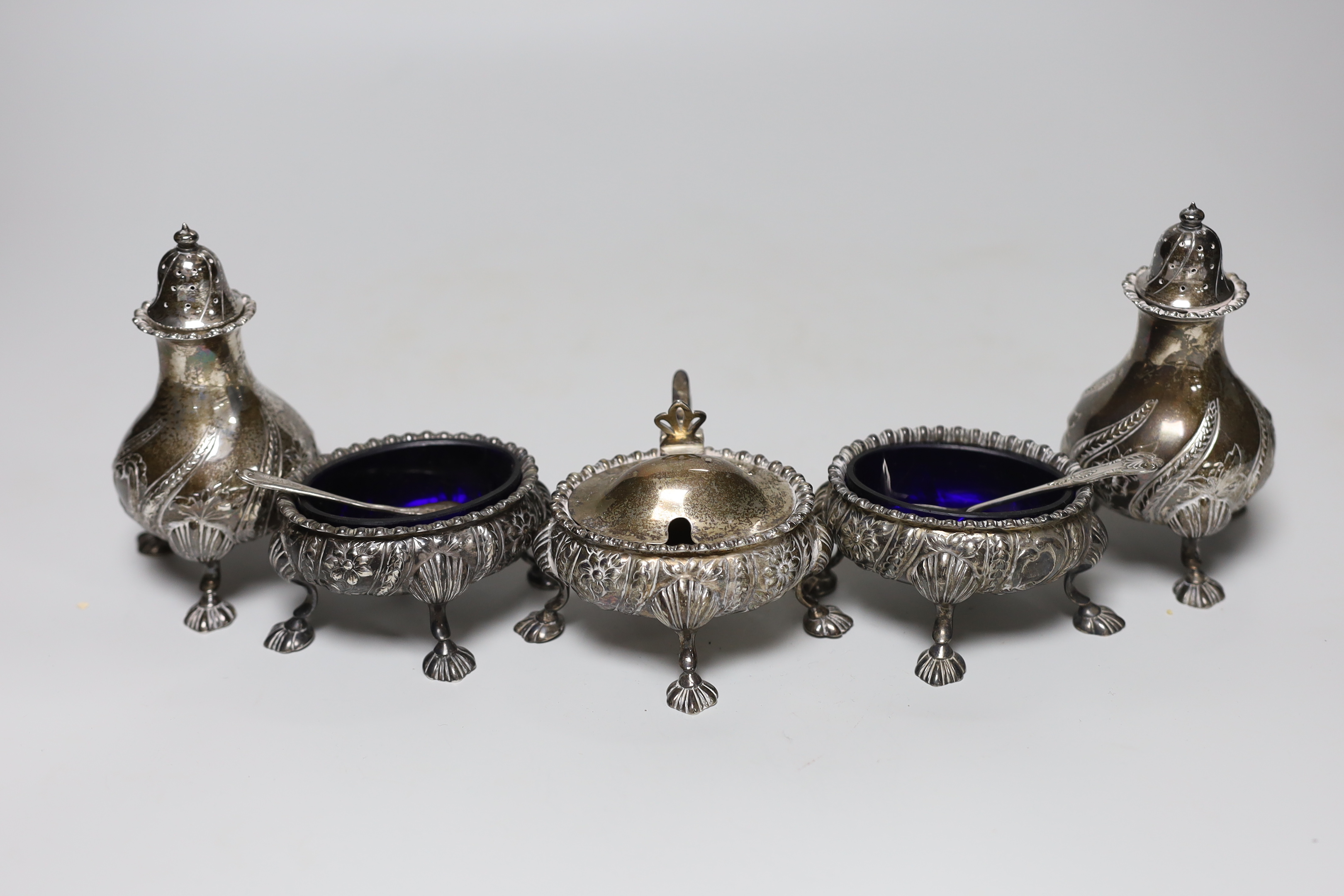 A George V five piece silver condiment set, William Hutton & Sons, Sheffield, 1928, with two associated spoons, one plated.
